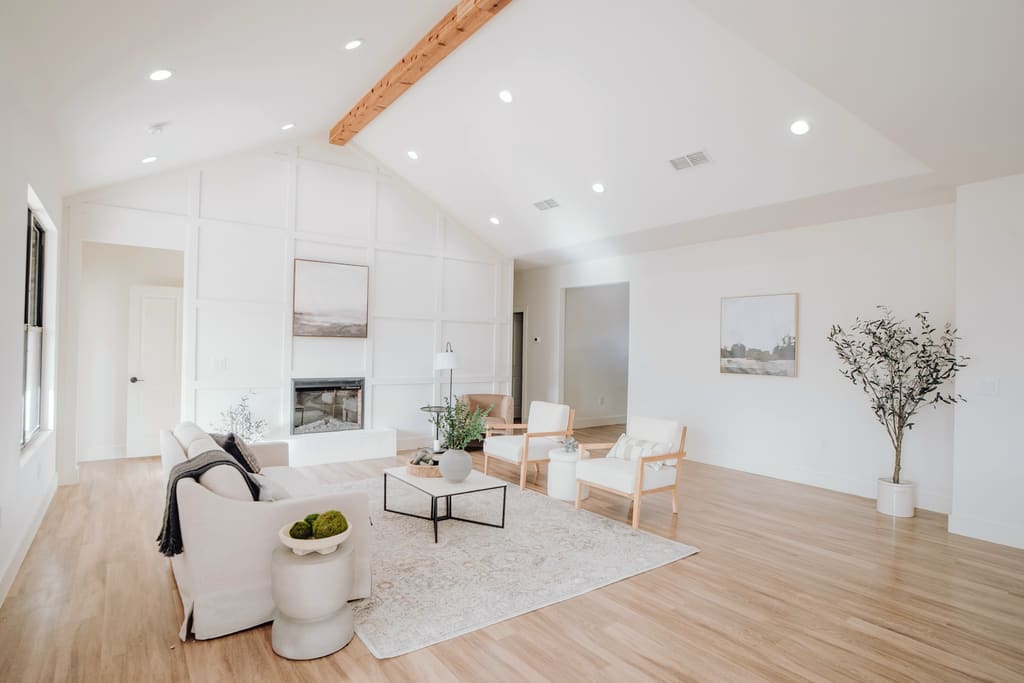 Bright, airy living room with crisp white board-and-batten walls, a vaulted ceiling with a wood beam, light oak floors and neutral furniture